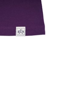 Lila Baumwoll-T-Shirt-Hemd mit einem gewebten Etikett. Das Etikett zeigt gekreuzte Utensilien und die Buchstaben "B R" in Schwarz auf weißem Hintergrund.