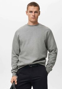 Sudadera gris de cuello redondo hecha de tela suave, con mangas largas y un corte relajado, combinada con pantalones negros. Diseño simple y funcional.