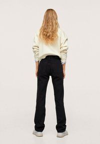 Jeans neri a gamba dritta, abbinati a un felpa oversize color crema, mostrati da dietro. Tessuto morbido, vestibilità casual.