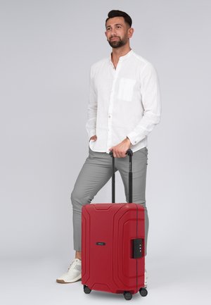 Roter Hartschalenkoffer mit strukturierten Oberflächen, versenkten Rädern, ausziehbarem Griff und einem Zahlenschloss. Ideal für Reisen.