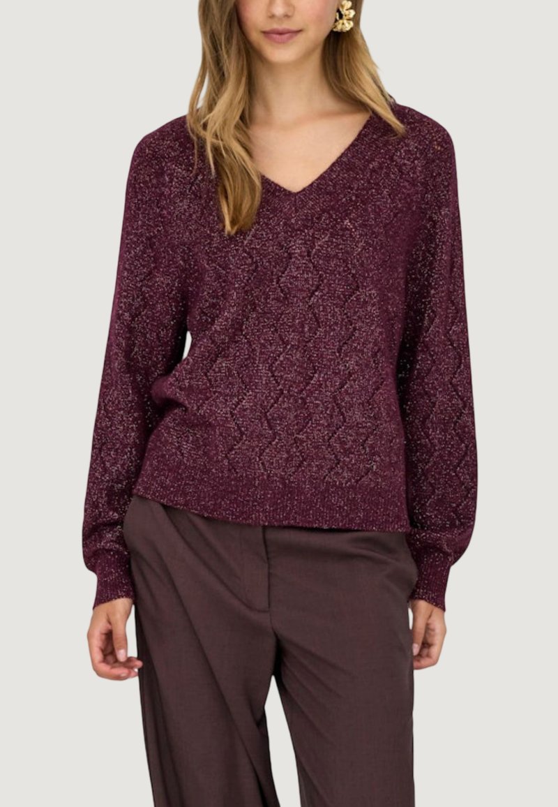 Maglione a V con maniche lunghe in un ricco color bordeaux con un motivo a diamante testurizzato, realizzato in un filato lucido. Abbinato a pantaloni marroni dalla vestibilità ampia.