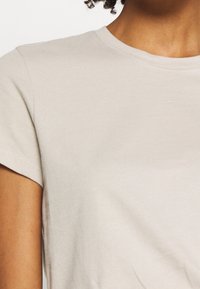 Camiseta de algodón beige con mangas cortas y escote redondo. Textura suave y diseño sencillo sin patrones ni adornos.