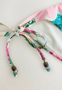 Gros plan d'un bas de bikini floral rose, blanc et multicolore avec nouette et perles en bois sur un fond clair.