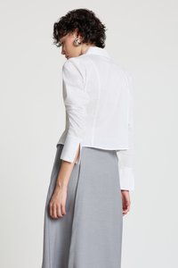 White cropped shirt with long sleeves and side slits, paired with a gray skirt. Smooth fabric texture, classic collar, and buttoned cuffs.