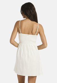 Λευκό φόρεμα με σφηκοφωλιά κορσάζ και λεπτές ρυθμιζόμενες τιράντες, με φουσκωτή φούστα που πέφτει πάνω από τα γόνατα. Ομαλή υφή υφάσματος.