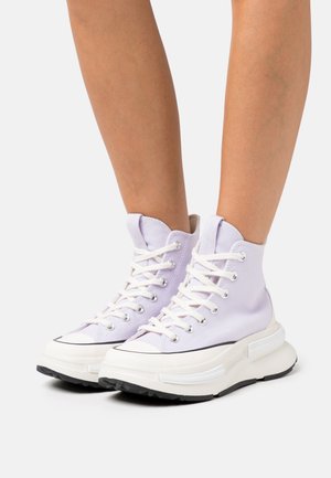 Sneakers alta in canvas lavanda chiaro, con lacci bianchi, puntale in gomma nera a contrasto e suola bianca spessa.