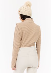 Gestreepte beige pullover met hoge kraag en lange mouwen. Bevat een structuurbreipatroon en gladde beige broeken. Gehaakte crèmekleurige beanie met pompon.