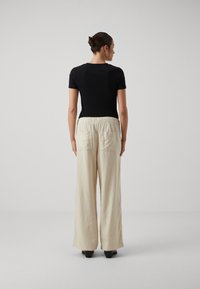 Top nero aderente a maniche corte abbinato a pantaloni larghi color crema con elastico in vita e due tasche posteriori.