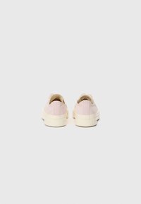 Light pink canvas sneakers with a low-profile design, white rubber sole, and no visible hardware, focusing on a smooth texture.