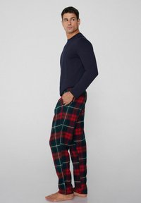Granatowa koszulka z długim rękawem w połączeniu z zielono-czerwonymi pidżamowymi spodniami w kratę. Spodnie mają luźny krój, kieszenie oraz białe linie w krateczkę.