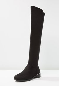 Botas negras por encima de la rodilla hechas de un material suave similar a ante, con punta redondeada y tacón bajo de bloque. Diseño sin costuras sin hardware visible.