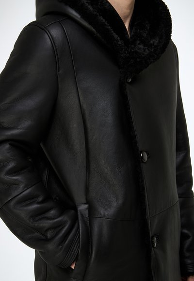Schwarzer Ledermantel mit einer weichen, schwarz pelzgefütterten Kapuze, ausgestattet mit Knopfverschluss, Seitentaschen und einer glatten, strukturierten Oberfläche.