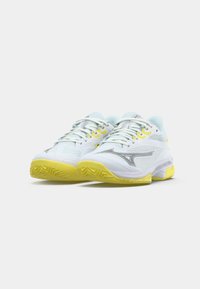 Tennis shoes with a white synthetic upper, yellow rubber outsole, and blue accents. Features a streamlined design and textured patterns.