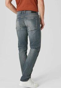 Blå denimjeans med avsmalnande ben, subtila blekningar, två bakfickor och en svart läderetikett i midjan, kombinerat med vita sneakers.