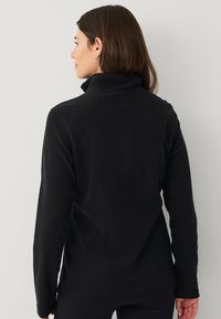 Zwarte fleecetop met een hoge kraag, lange mouwen en een zachte textuur, met een eenvoudig, strak ontwerp zonder zichtbare patronen.