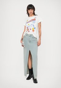 White t-shirt with colorful graphic print featuring flowers and illustrations, paired with a light blue denim maxi skirt with a front slit. Black ankle boots.