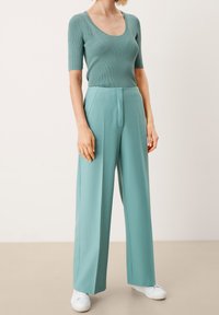 Ljus teal ribbad t-shirt med kort ärm i kombination med högmidjade byxor med vida ben i matchande färg. Vita sneakers fulländar outfiten.