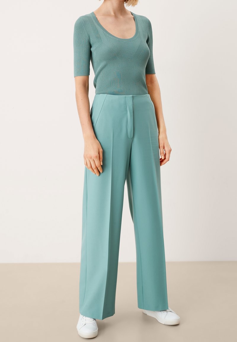 Ljus teal ribbad t-shirt med kort ärm i kombination med högmidjade byxor med vida ben i matchande färg. Vita sneakers fulländar outfiten.