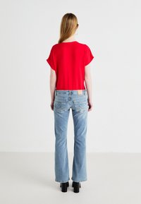 Red short-sleeve top with a rounded neckline, paired with light blue, flared jeans featuring back pockets and a tan leather patch. Black heeled boots.