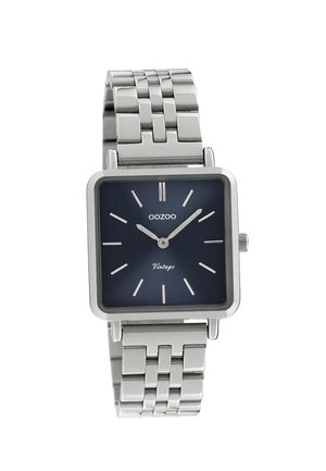 Quadratische silberne Metalluhr mit einem navyblauen Zifferblatt, silbernen Stundenmarkierungen und einem Kettenarmband. Besitzt ein markantes minimalistisches Design.