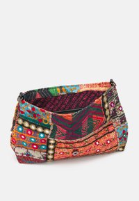 Barevná látková taška s různými vzory, texturami a dekorativními ozdobami. Má zipové uzavření a kulatý tvar.