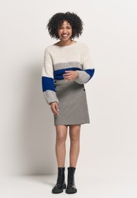 Sweter dzianinowy w kremowe, szare i niebieskie paski; mini spódnica w szary w kratę houndstooth z detalami w postaci guzików; czarne lace-up buty wojskowe.