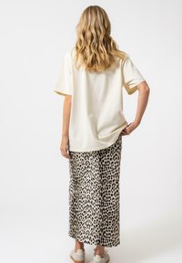 Haut crème à manches courtes associé à une longue jupe imprimée léopard, mettant en valeur une texture douce et un design fluide. La chaussure a une couleur claire et un style simple.