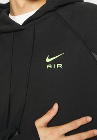 Svart huva sweatshirt med en Nike-logotyp och "AIR" i neongrönt på bröstet. Mjuk tyg, ribbade mudd och rak nederkant.