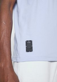 Camiseta de algodón de color azul claro con una etiqueta negra cosida en el lado inferior, con detalles blancos y cuello redondo, diseño ajustado.