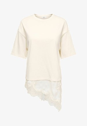 Haut court à manches courtes crème avec encolure ronde et ourlet en dentelle asymétrique plus long d'un côté.