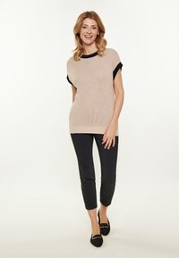 Fényes rózsaszín kötött felső fekete bordázott részletekkel, vékony fekete nadrággal és fekete lapos talpú cipővel párosítva. Rövid ujjak, laza szabású dizájn.