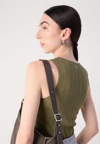 Oliven grønn strikket tanktop med rillete teksturer og logo detaljer på baksiden, parret med en brun skulderveske.