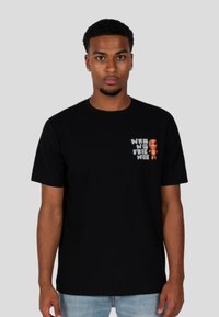 Černé bavlněné tričko s grafikou na levé straně hrudi a frází "ŠPATNÍ PŘÁTELÉ" a oranžovým designem postavy. Krátké rukávy a kulatý výstřih.