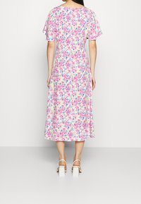 Robe midi fleurie aux couleurs pastel avec des manches courtes volantées, un tissu léger et une silhouette fluide. Sandales blanches à talon carré remarquables.