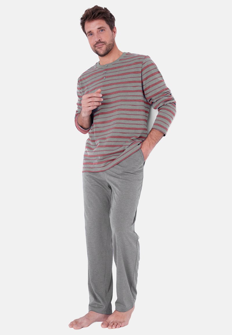 Grijze langemouwshirt met rode horizontale strepen en drie knopen; gecombineerd met grijze broek, beide in een zachte stof. Model staat op blote voeten.