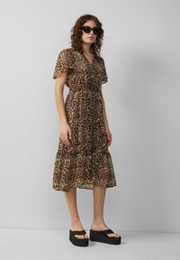 Luipaardprint, midi-jurk met korte mouwen en gelaagde voering in transparante stof met een getailleerde taille. Gemaakt met zwarte platform sandalen en oversized zonnebril.