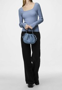 Haut à manches longues côtelé bleu clair associé à un pantalon large noir. Une petite pochette bleue à cordon est tenue par la personne. Texture lisse.