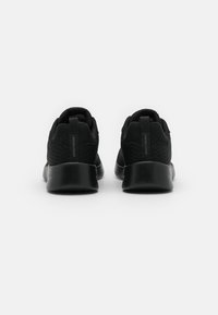 Zapatillas deportivas negras con una parte superior de malla texturizada, perfil bajo, lengüetas en el talón y suelas acolchadas negras, vistas desde atrás.
