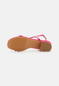 Rosa högklackad sandal med rem och spänndetalj, med en strukturerad gummisula och slät övre material. Rund tådesign.
