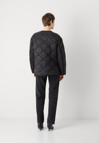 Čierna prešívaná puff jacket s okrúhlym výstrihom, textúrovaným vzorom a elastickými manžetami, v kombinácii s tmavými džínsy a elegantnými čiernymi podpätkami.