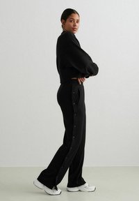 Sort cropped sweatshirt parret med sorte bukser med sideskigher. Skoene er hvide med et chunky design. Glat tekstur, afslappet design.