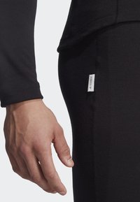 Black long-sleeve shirt with a soft, textured finish. Close-up of a hand near the side seam, featuring a small white label with "TERREX."
