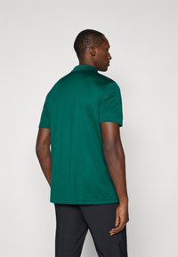 Tmavozelená polo košeľa s klasickým golierom a krátkymi rukávmi, vyrobená z hladkej, priedušnej tkaniny. Má rovný lem a jemné prešitie.