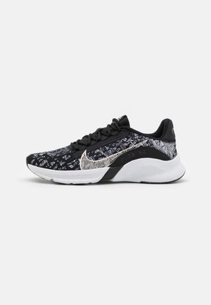Chaussure de course Nike à motif noir et blanc avec lacets noirs et semelle blanche, vue de profil sur un fond uni.
