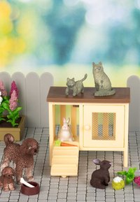 Speelgoed dieren set met een gele huisje voor huisdieren met bruine accenten, twee groene katten, een witte konijn en een bruine konijn, omringd door bloemen.