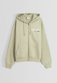 Felpa con zip di colore verde oliva, realizzata in cotone, con tasca a marsupio, coulisse sul cappuccio e grafica testuale bianca sul petto.