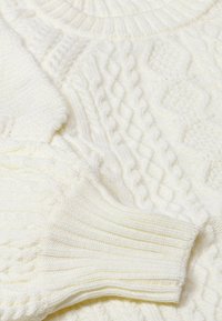 Hvid strikket sweater med strukturerede kabelmønstre og ribbede mansjetter. Stoffet ser blødt ud med et hyggeligt, chunky design.