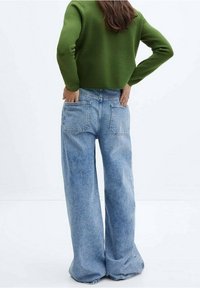 Pull vert court associé à un jean bleu clair à jambes larges, avec deux poches arrière et une coupe décontractée. Textures lisses visibles.