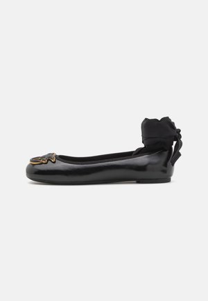 Ballerine in vernice nera con punta tonda, un dettaglio decorativo con logo nella parte anteriore e un morbido fiocco in raso nero sul tallone.