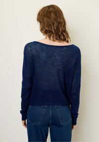 Granatowy, lekki sweter z dzianiny o luźnym kroju, szerokim dekolcie i długich rękawach, zestawiony z jeansami o wysokim stanie.